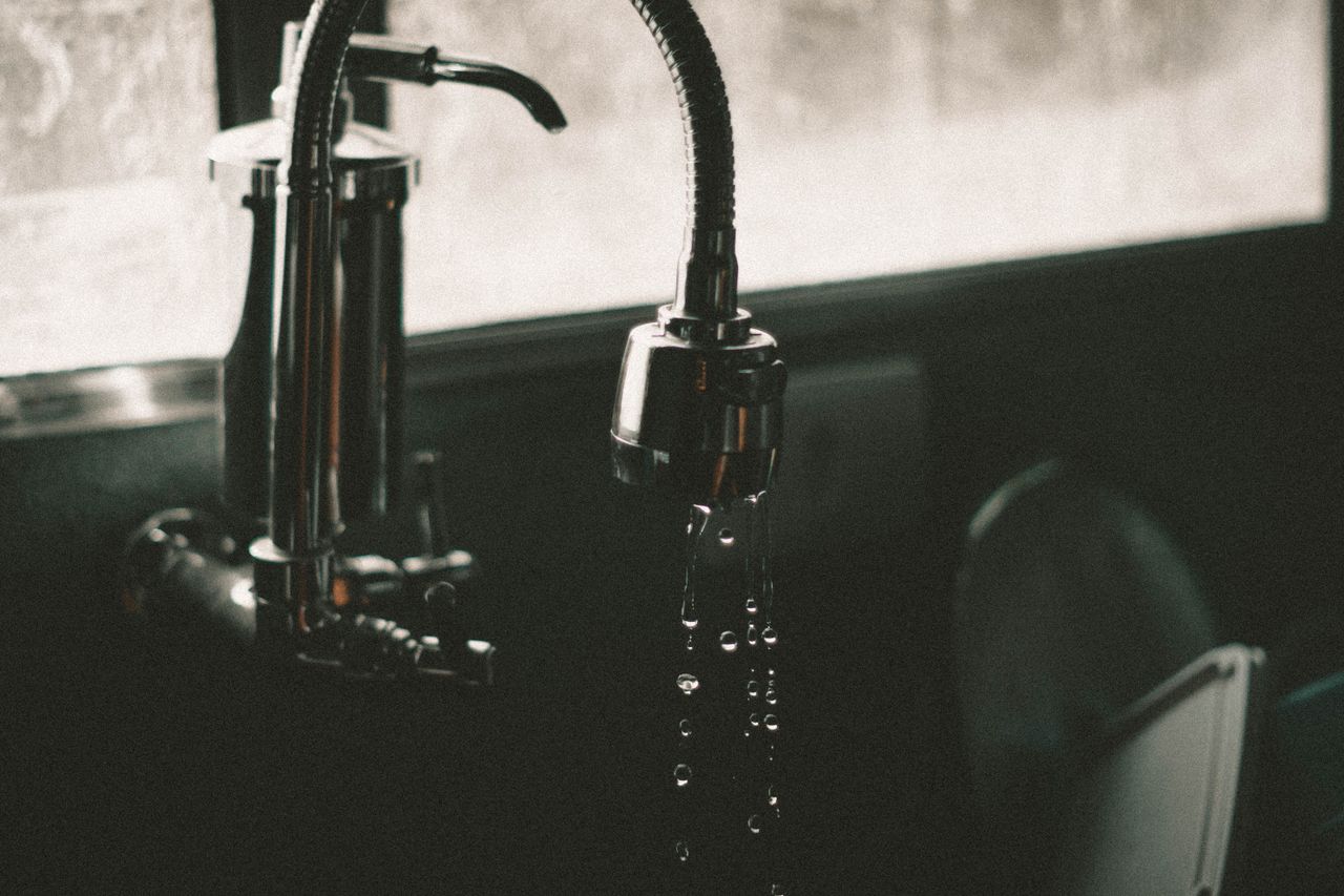 Close-up of a kitchen faucet with water droplets falling into the sink, captured in a minimalist style.